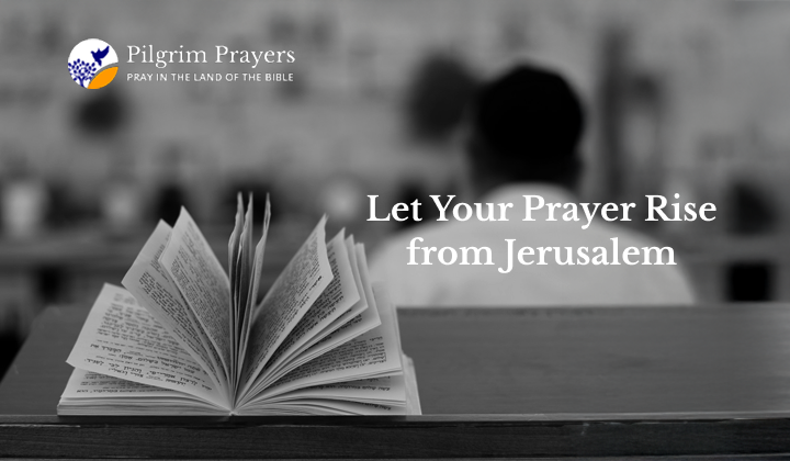 Hands folded in prayer beside a Bible and laptop, symbolizing faith and online prayer connection to Jerusalem.