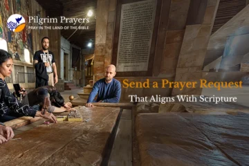 Bible open on a table with hands folded in prayer, representing sending a prayer request aligned with Scripture.