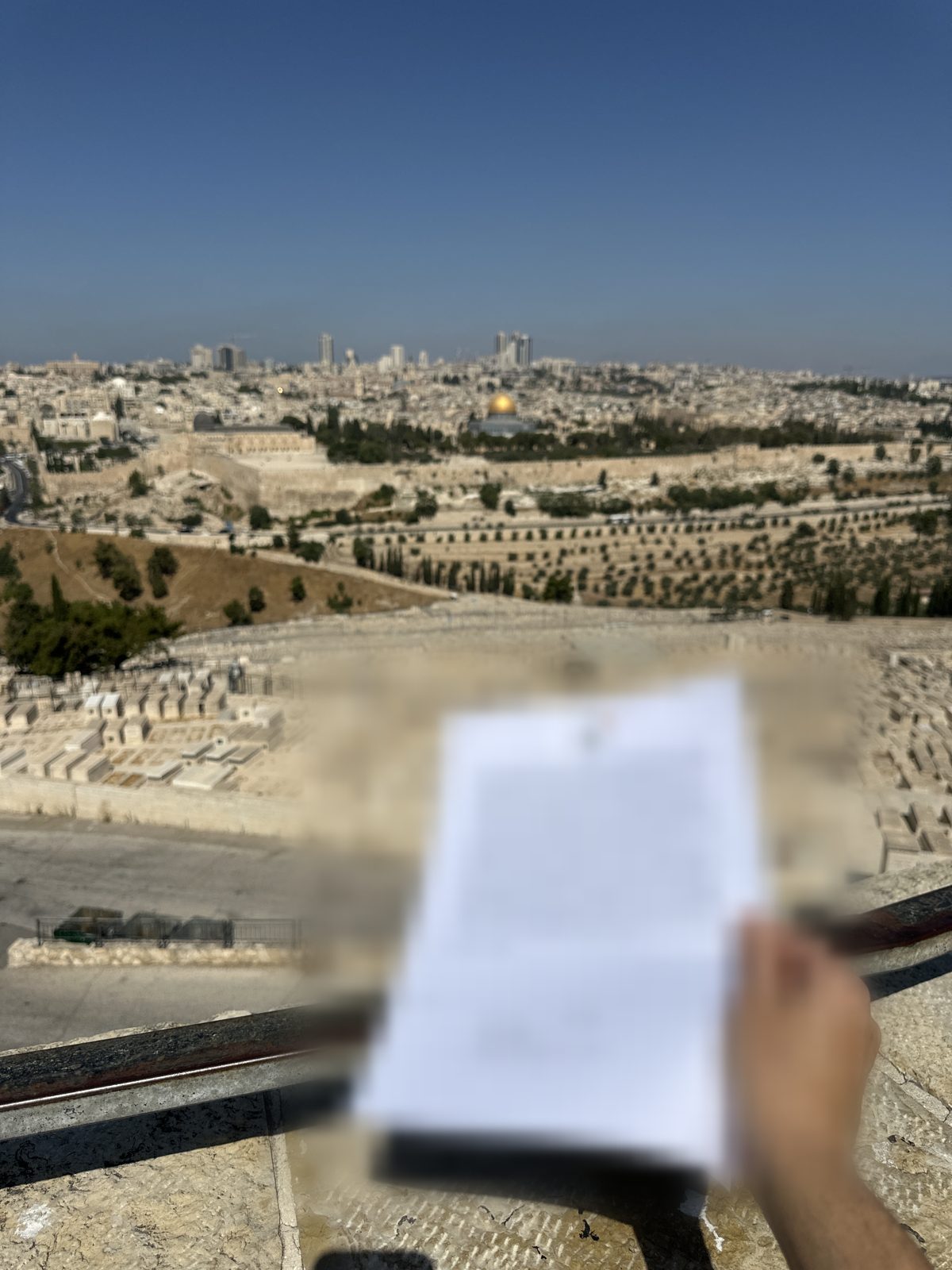 A printed prayer held at the Mount of Olives overlook, with the Old City of Jerusalem and the Dome of the Rock behind
